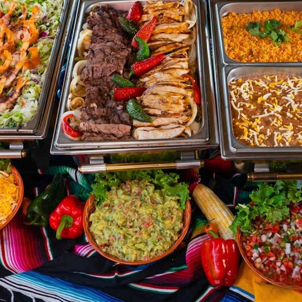 A vibrant Mexican buffet with fajitas, rice, beans, guacamole, and salsa on a colorful serape.